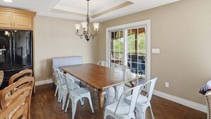 A dining area with a wooden table and chairs, a chandelier, and a view through a glass door. - Perfect Lake Life at Bulldog Lake House! Huge Dock, Dock Bar, Decks & Fun at 2mm! (Lake Ozark)