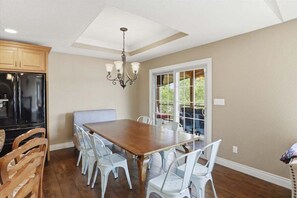 A dining area with a wooden table and chairs, a chandelier, and a view through a glass door. - Perfect Lake Life at Bulldog Lake House! Huge Dock, Dock Bar, Decks & Fun at 2mm! (Lake Ozark)
