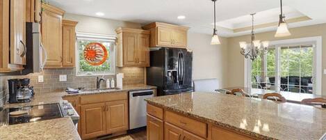 A kitchen with wooden cabinets, granite countertops, a black refrigerator, and a dining area with chairs.