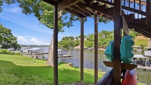 A riverside view with a wooden deck, a bridge, and a boat dock. - Flat Lakefront Retreat With Private Dock & Kayaks (Lake Ozark)