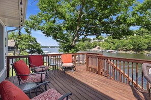 Eine Holzterrasse mit Gartenmöbeln, Blick auf einen See und ein Baum.