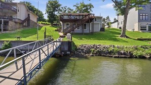 A residential area with a bridge over a body of water, a small building with a staircase, and houses with balconies. - Flat Lakefront Retreat With Private Dock & Kayaks (Lake Ozark)