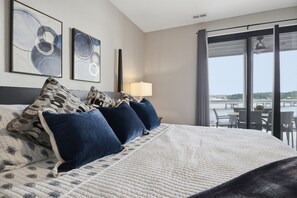 Ein Hotelzimmer mit einem großen Bett, zwei an der Wand befestigten Kunstwerken, einem Nachttisch mit einer Lampe und Blick ins Freie durch eine Schiebetür.