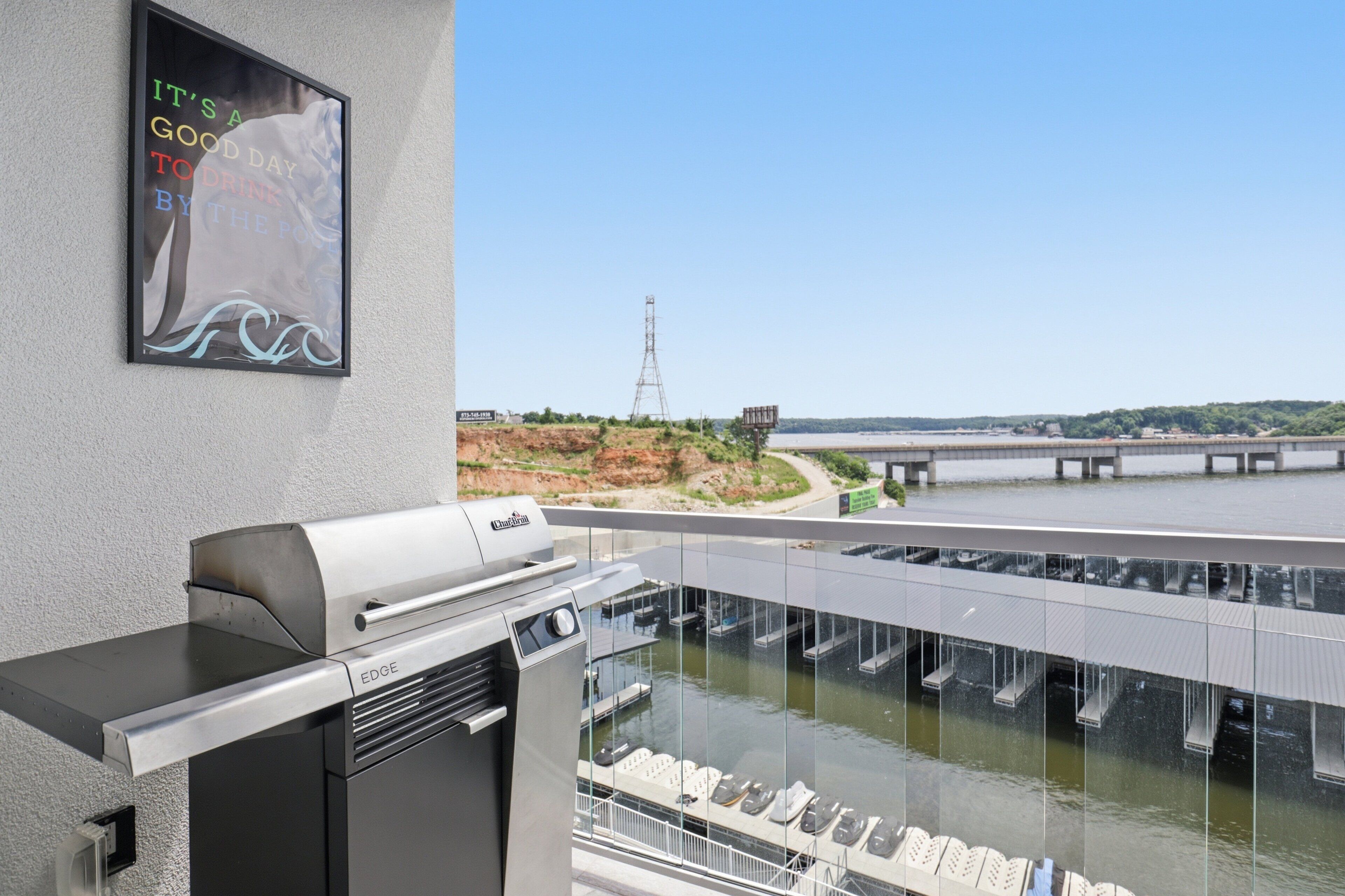 Un balcon avec un barbecue, une affiche et une vue sur un pont et l’eau.