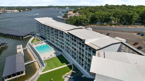 A modern hotel with a large glass facade, a swimming pool, and a view of a river. - Main Channel Views, Resort Pools & Boat Slip at Topsider's 19mm (Osage Beach)