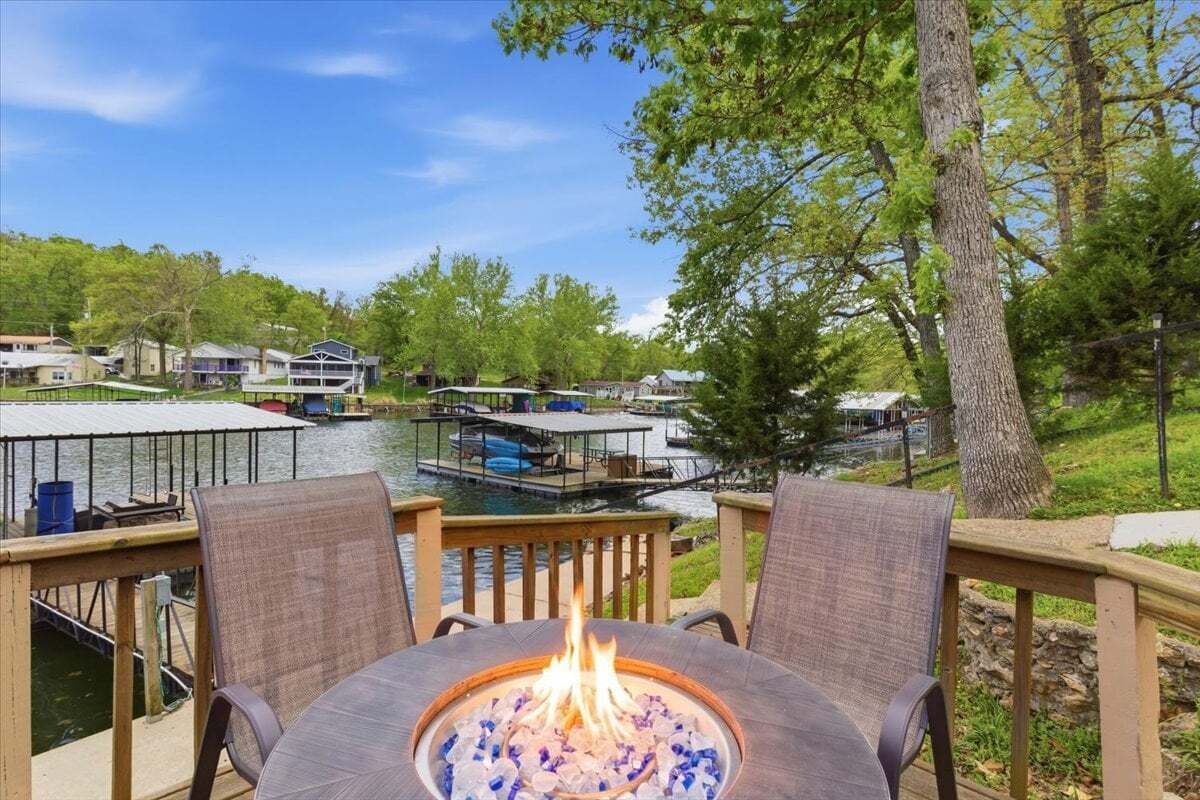 A deck with a fire pit, overlooking a lake with boats and houses.
