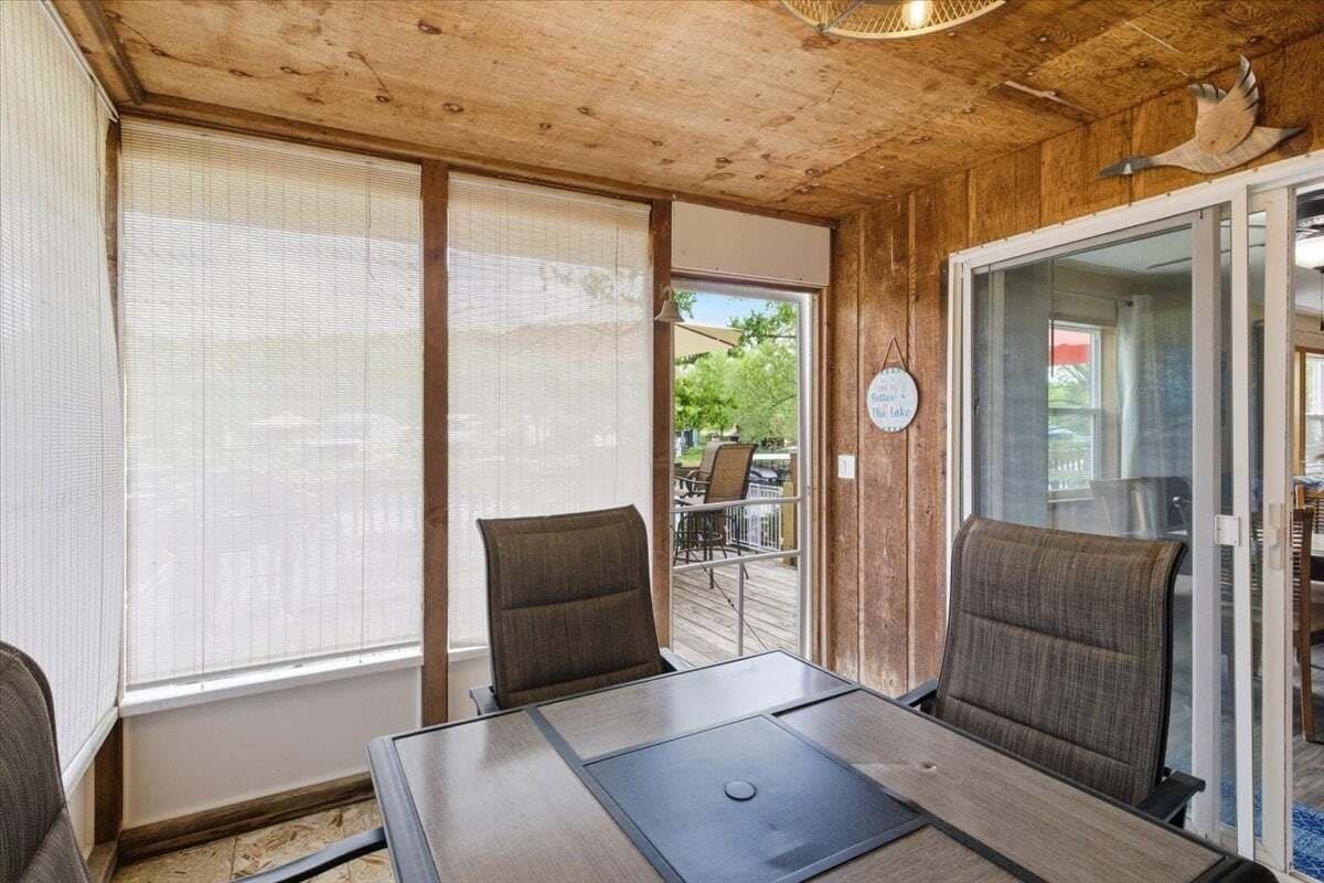 Een kamer met een houten plafond, twee stoelen, een tafel en een glazen schuifdeur naar buiten.