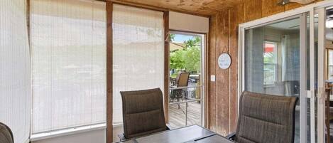 A room with a wooden ceiling, two chairs, a table, and a sliding glass door leading outside.