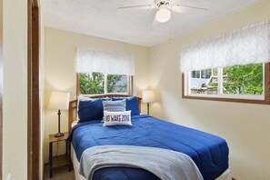 A bedroom with a bed, two bedside lamps, a ceiling fan, and a window with a view of greenery. - Lakefront Fun With Private Dock, Firepit, Swim Mat, Kayaks & Screened Lake Room (Gravois Mills)