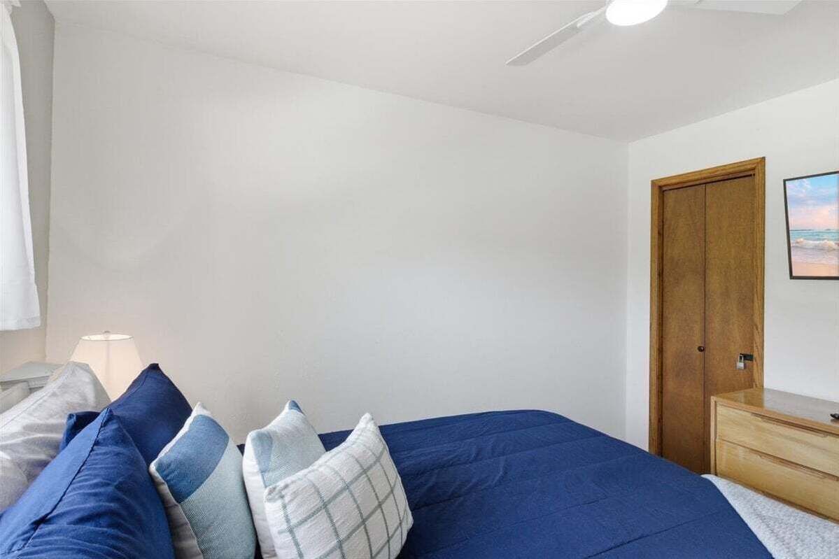 A bedroom with a bed, pillows, a wooden dresser, a nightstand, a lamp, and a door.