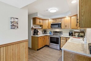 A compact kitchen with wooden cabinets, a microwave, an oven, and a sink. - Lakefront Fun With Private Dock, Firepit, Swim Mat, Kayaks & Screened Lake Room (Gravois Mills)