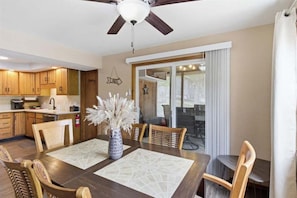 A dining area with a table, chairs, a vase with dried flowers, a ceiling fan, and wooden cabinets. - Lakefront Fun With Private Dock, Firepit, Swim Mat, Kayaks & Screened Lake Room (Gravois Mills)