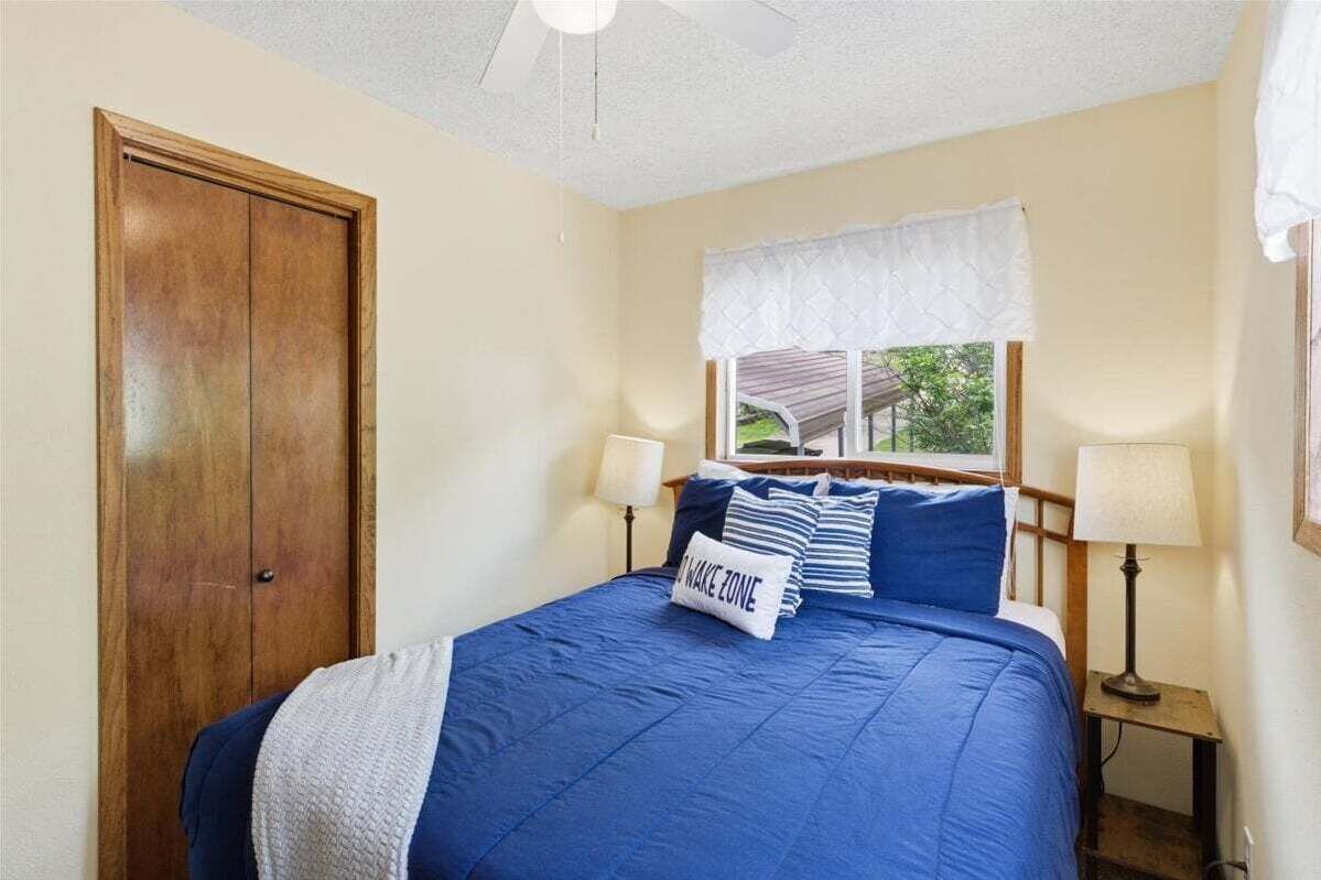 Un dormitorio con una cama, dos lámparas de noche, un ventanal con un valance blanco y una puerta de madera.