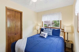 Un dormitorio con una cama, dos lámparas de noche, un ventanal con un valance blanco y una puerta de madera.
