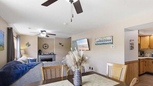 A room with a bed, a dining table with placemats, a TV, a wall clock, and a sign that reads 'LAKEHOUSE'. - Lakefront Fun With Private Dock, Firepit, Swim Mat, Kayaks & Screened Lake Room (Gravois Mills)