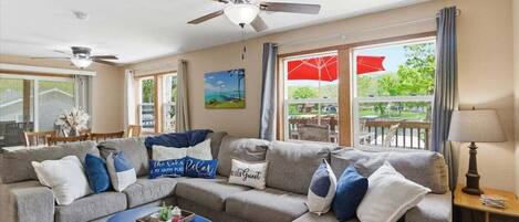 A living room with a sofa, a coffee table, and a ceiling fan. There is a window with a view of the outdoors.