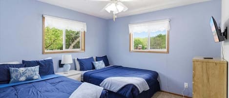 Un dormitorio con dos camas, un ventilador de techo, un armario de madera y una ventana con vistas a árboles.