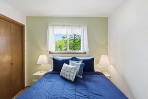 A bedroom with a bed, two bedside lamps, a window with a view of trees, and a wooden wardrobe. - Lakefront Fun With Private Dock, Firepit, Swim Mat, Kayaks & Screened Lake Room (Gravois Mills)