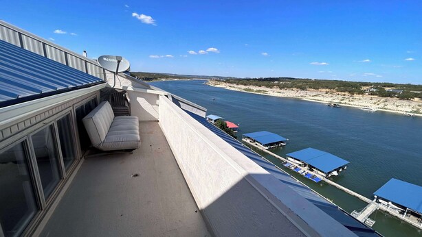 Un balcón con vistas al agua, una zona de estar con sofá y un espacio cubierto con mesas.