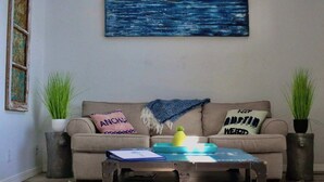 Una sala de estar con un sofá, dos mesitas auxiliares, una mesa de centro y un cuadro en la pared.