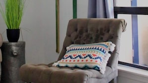 Una habitación con un sillón capitoné, un cojín estampado, una planta en maceta y dos palas de madera en la pared.