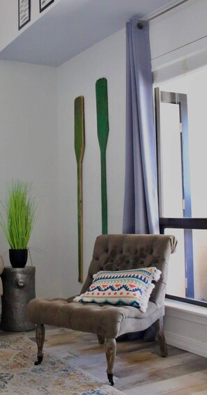 A room with a tufted armchair, a patterned cushion, a potted plant, and two wooden paddles on the wall. - Right on the water! Lake Travis (Spicewood)