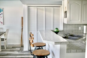 A kitchen with a white countertop, a sink, and a green vase. There are wooden chairs and a table. - Right on the water! Lake Travis (Spicewood)