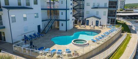 A hotel with a pool area, including lounge chairs and a hot tub.