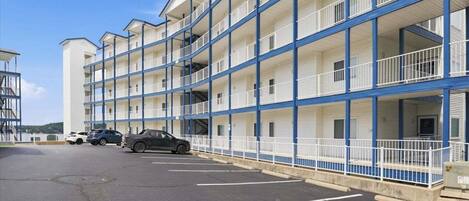 A multi-story motel with balconies, a parking lot, and a clear sky.