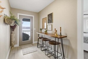 Een keuken met een houten bar, twee krukken, een hangende plant en lijstwerken aan de muur.