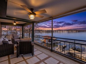 Ein Balkon mit Korbmöbeln, einem Deckenventilator und Blick auf ein Gewässer im Abendlicht.