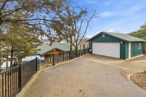 A single-story building with a green garage door, a covered porch, and a fenced driveway. - Outdoor Dream Lakefront Home w/ Private Dock, 2 Slips & Kayak (Sunrise Beach)
