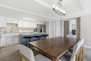 Een moderne keuken met witte kasten, een grote houten eettafel en barstoelen.