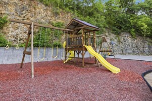Un parque infantil con una estructura de madera, un tobogán amarillo y columpios.