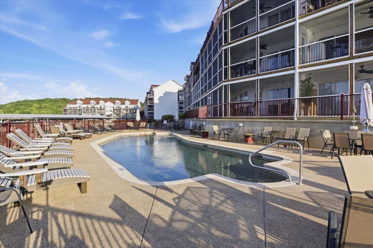 A pool area with lounge chairs, a pool, and a building with balconies.