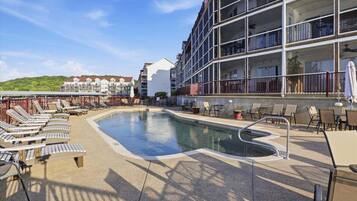 A pool area with lounge chairs, a pool, and a building with balconies.