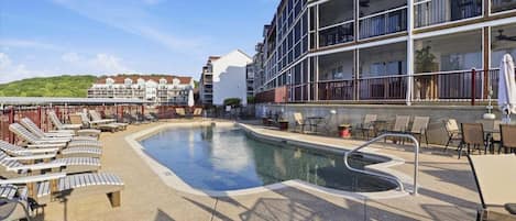 Un área de piscina con sillas de descanso, una piscina y un edificio con balcones.
