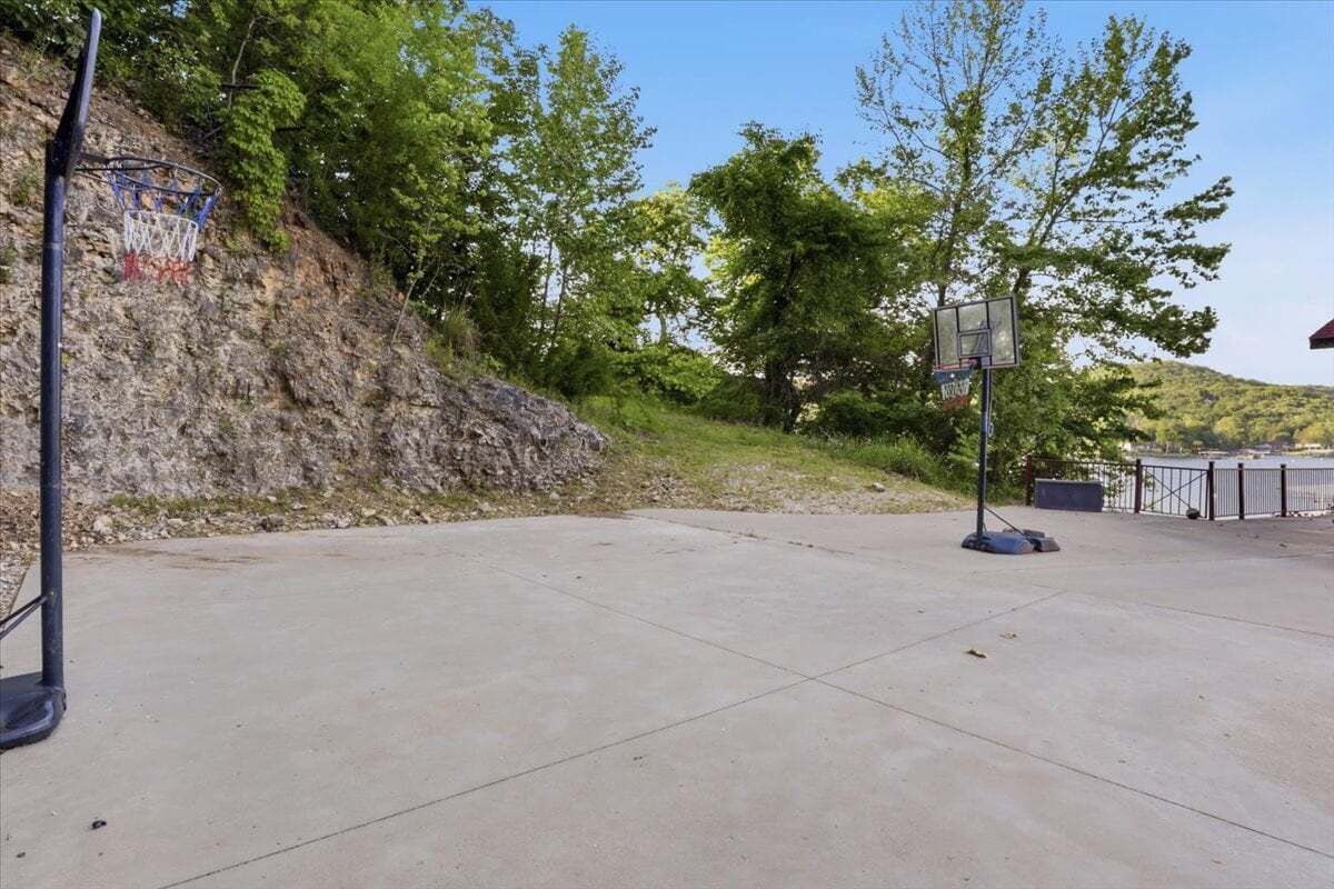 Una cancha de baloncesto al aire libre con superficie de hormigón, dos aros de baloncesto y un promontorio rocoso al fondo.