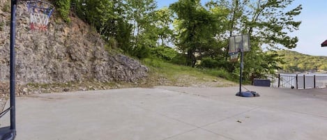 Una cancha de baloncesto al aire libre con superficie de hormigón, dos aros de baloncesto y un promontorio rocoso al fondo.