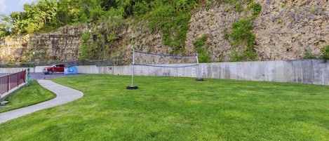 Un césped bien cuidado con una red de voleibol, un muro de concreto y un vehículo rojo estacionado cerca.