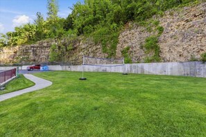 A well-maintained grassy area with a volleyball net, a concrete wall, and a red vehicle parked nearby. - Lakefront on Big Niangua, 2 Heated Pools, Boat Slip, Fire Pit, & Big Views (Camdenton)