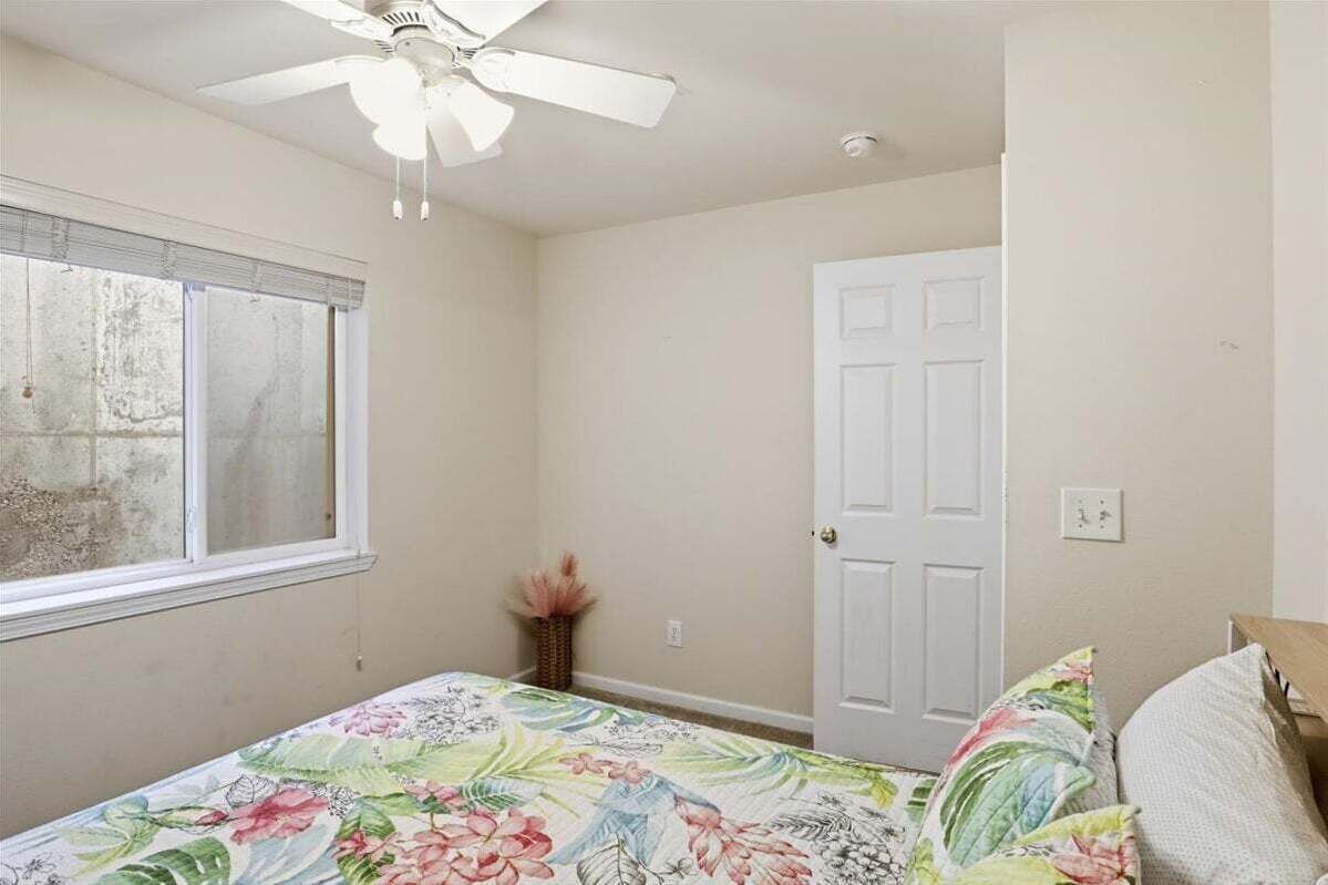 Un dormitorio con una cama, ventilador de techo, ventana y puerta.