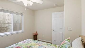 Un dormitorio con una cama, ventilador de techo, ventana y puerta.