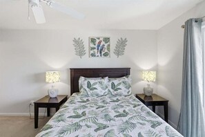 Quarto com cama, duas mesas de cabeceira com luminárias, ventoinha no teto e quadro na parede.