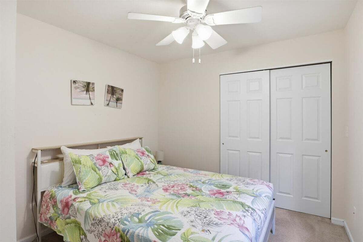 Ein Schlafzimmer mit Bett, Deckenventilator, Tür und zwei an der Wand befestigten Bildern.