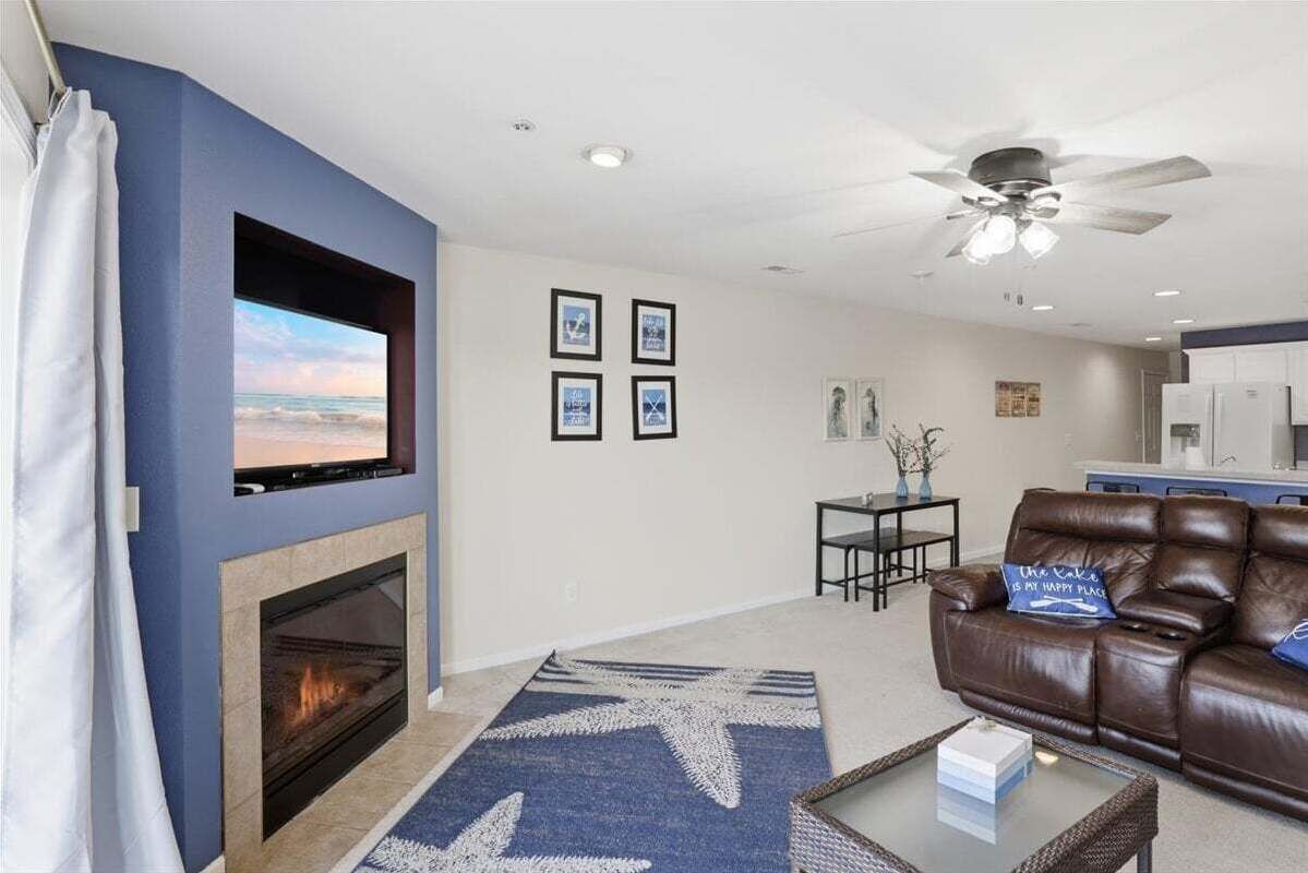 A living room with a fireplace, a television mounted on the wall, a brown leather sofa, and a ceiling fan.