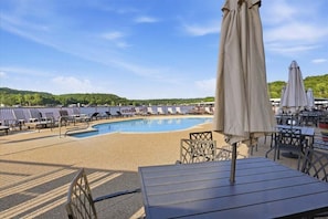 Un espace aménagé au bord de la piscine, avec des chaises longues et des parasols, une piscine, et une vue sur des collines en arrière-plan.