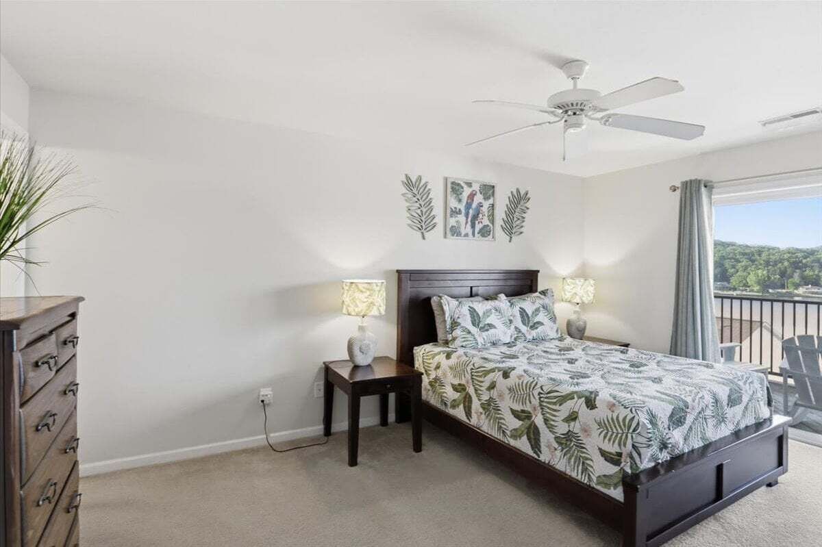 Un dormitorio con cama, lámparas de noche, ventilador de techo, cómoda y vistas por la ventana.