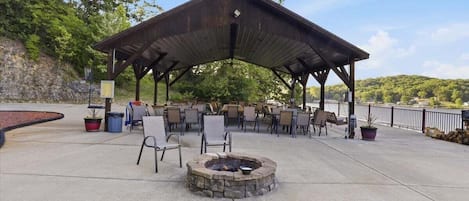 An outdoor patio with a covered seating area, a fire pit, and a view of a lake.