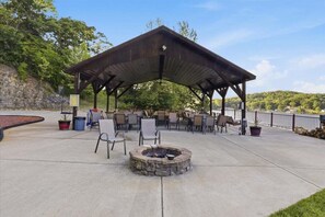 Un patio exterior con zona de estar cubierta, una chimenea y vistas a un lago.